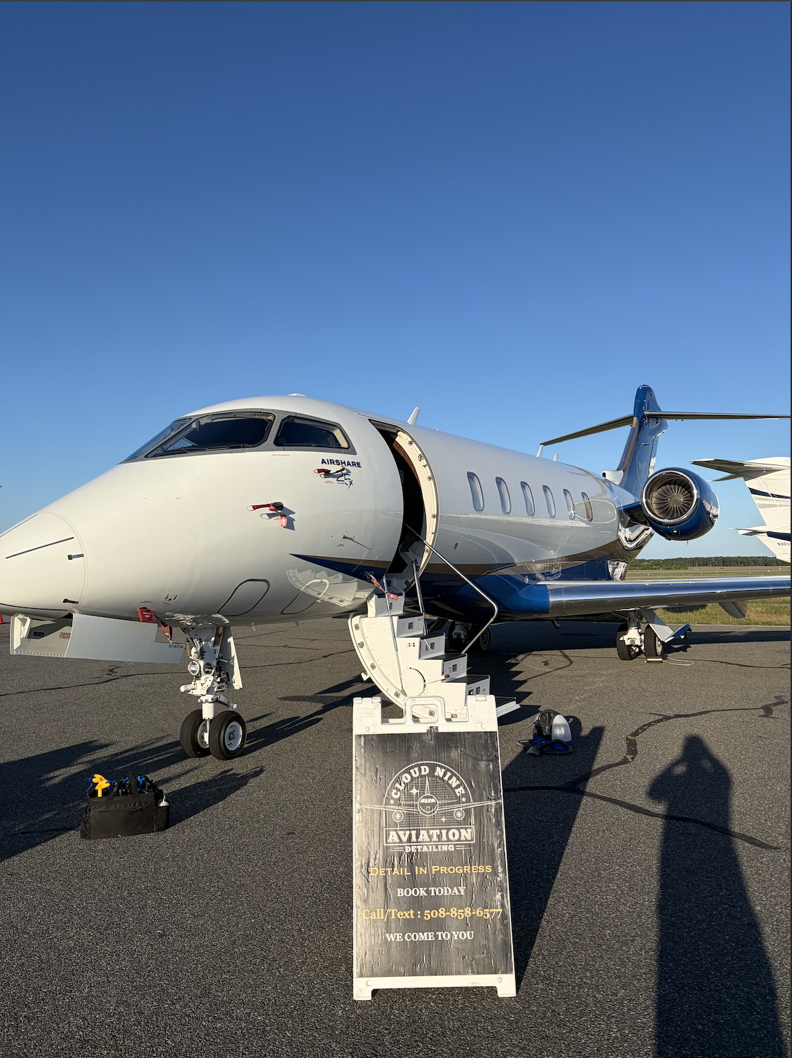 Blue and white business jet on the ramp beside a Cloud Nine Aviation detailing sign